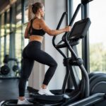 Atleta usando elíptico profissional em academia moderna com luz natural e fundo desfocado